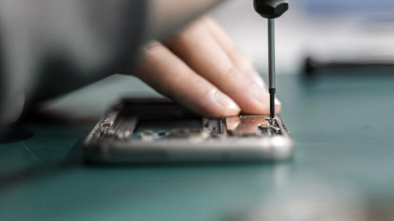 A person exercising their right to repair by opening a smartphone with a screwdriver.