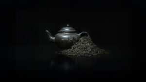 A black, Chinese-style pot of tea with a pile of lapsang souchong tea leaves beside it.