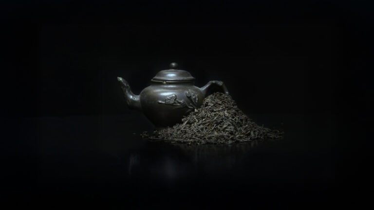 A black, Chinese-style pot of tea with a pile of lapsang souchong tea leaves beside it.
